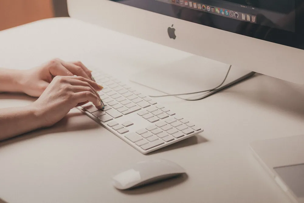 Une photo des mains d'une femme sur le clavier d'un Mac, sur le point d'écrire une proposition commerciale.